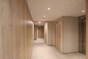 A corridor with wooden paneling, a tiled floor, and a ceiling with recessed lighting.
