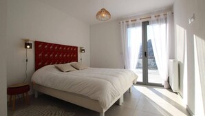 A bedroom with a bed, a red headboard, a window with curtains, and a view of the city.