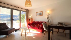 A modern living room with a red sofa, a dining table, and a large window offering a view of the outdoors.