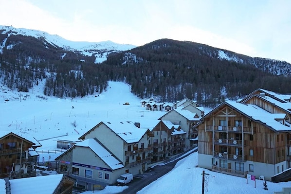 A snow-covered mountain village with wooden buildings, a ski slope, and a road.
