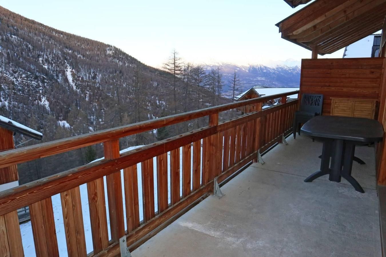 Un balcon en bois, doté d’une balustrade en métal, qui offre une vue sur un paysage montagneux enneigé.