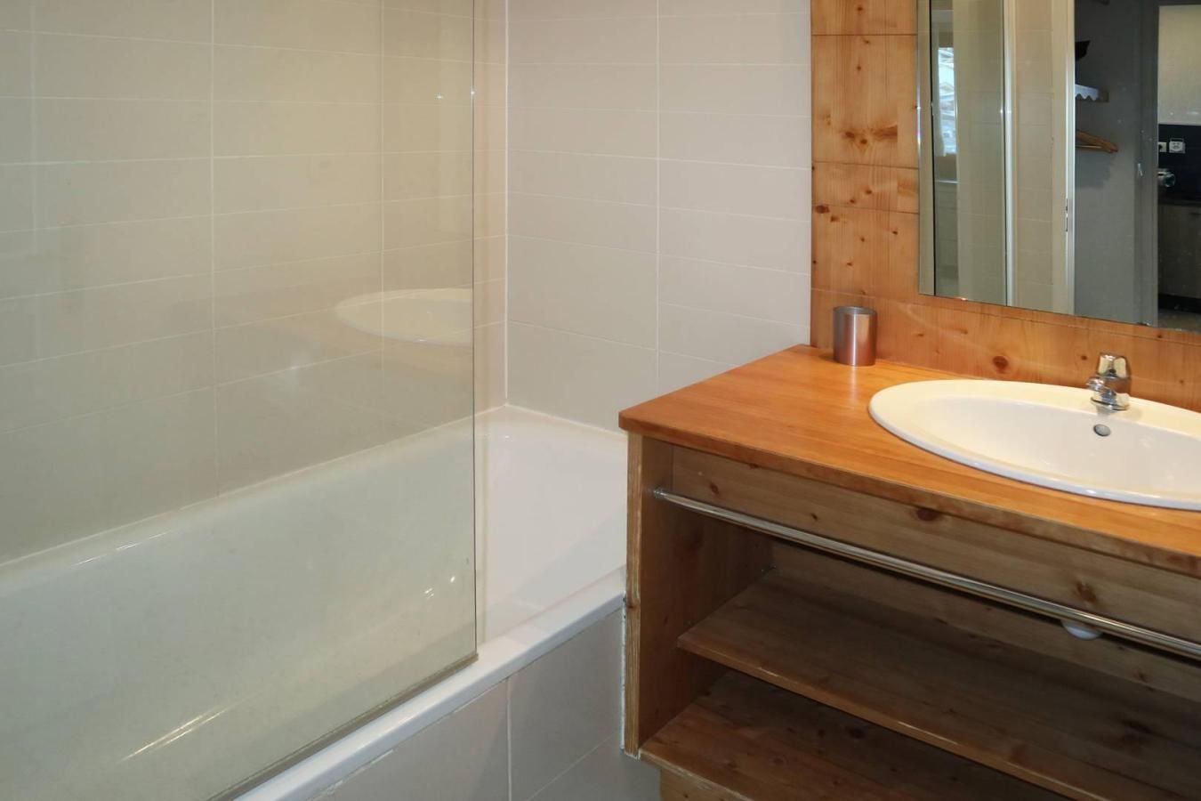 A bathroom with a bathtub, a wooden vanity with a sink, and a mirror.