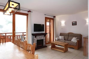 A living room with a fireplace, a television mounted on the wall, a wooden dining table with chairs, and a sofa.