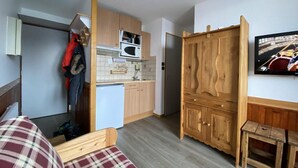 A compact room with a kitchenette, a bed with a plaid cover, a wooden wardrobe, and a television on the wall. - 100m from ski slopes, 1st floor, view mountain, balcony, tv, ski locker, 20m², Montalbert (Aime)