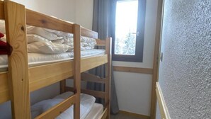 A small, narrow room with a bunk bed, a window with curtains, and a textured wall. - 100m from ski slopes, 1st floor, view mountain, balcony, tv, ski locker, 20m², Montalbert (Aime)