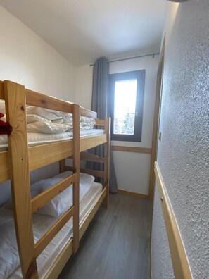 Ein kleiner, schmaller Raum mit einem Etagenbett, einem Fenster mit Vorhängen und einer strukturierten Wand.