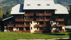 A two-story building with a metal roof and wooden balconies, set against a mountainous backdrop. - 100m from ski slopes, 1st floor, view mountain, balcony, tv, ski locker, 20m², Montalbert (Aime)