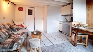 A cozy living room with a sofa, a small round table, and a kitchen area with cabinets and a dishwasher.