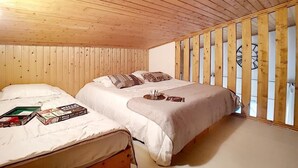 A room with a wooden ceiling and walls, a bed with a white mattress and beige bedding, and a window with vertical blinds.