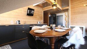 A cozy wooden interior with a dining table set for four, a black sofa, and a television mounted on the wall. - 3rd floor, tv, ski locker, 100m², Serre Chevalier (Briançon)