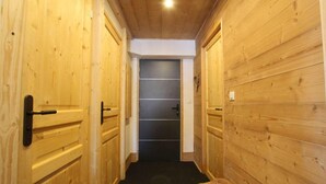 A narrow hallway with wooden walls and a dark floor, leading to a door with a black handle. - 3rd floor, tv, ski locker, 100m², Serre Chevalier (Briançon)