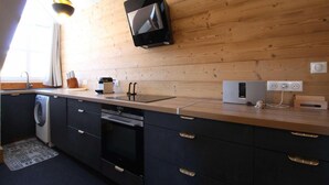 A modern kitchen with a wooden wall, a built-in oven, a dishwasher, and a flat-screen TV mounted above the counter. - 3rd floor, tv, ski locker, 100m², Serre Chevalier (Briançon)
