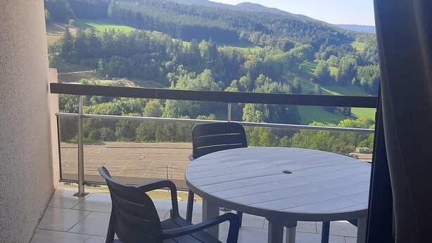A balcony with a round table and two chairs, overlooking a green valley with trees and hills. - 7th floor, balcony, parking, tv, 63m², Villard de Lans (Villard-de-Lans)