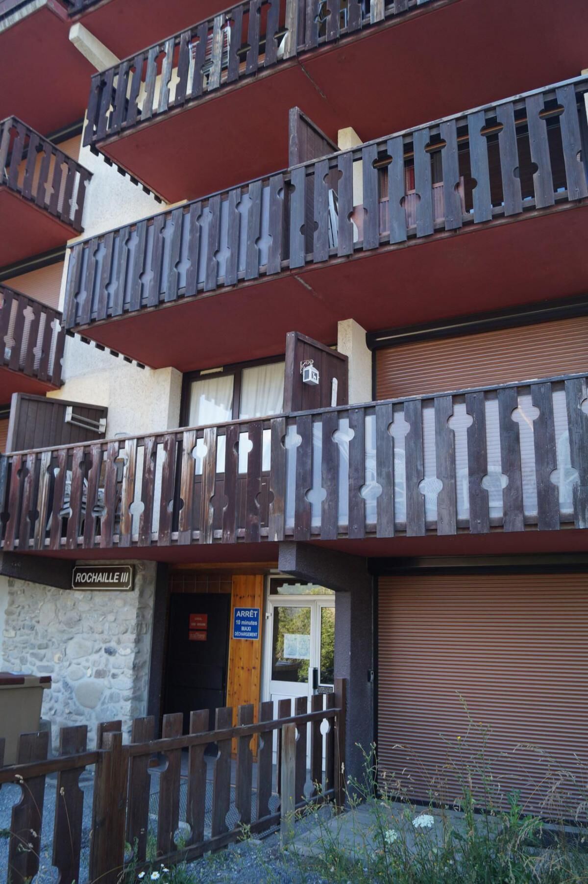 A multi-story building with balconies, a stone facade, and a closed shutter door.