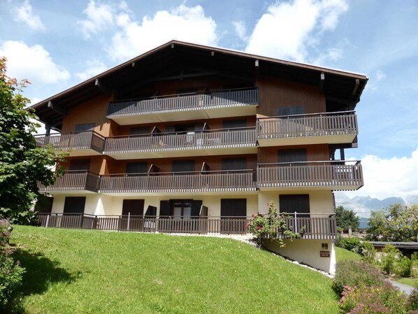 A multi-story building with balconies, a grassy lawn, and a mountainous backdrop. - 2nd floor, view mountain, parking, tv, ski locker, 26m², Combloux (Combloux)