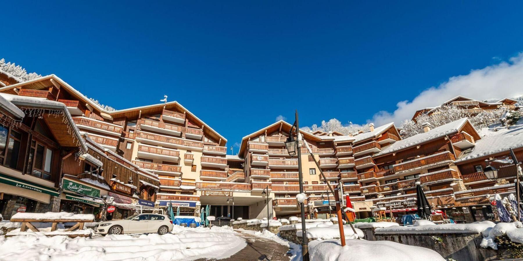Un complejo turístico en la montaña cubierto de nieve, con edificios de madera de varios pisos, un cielo azul despejado y una calle pavimentada.