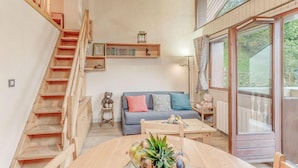 A cozy living room with a wooden staircase, a blue sofa, and a wooden dining table with a fruit centerpiece.