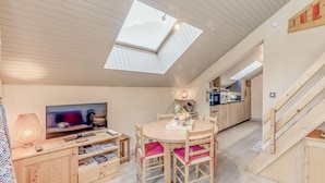 A cozy loft-style living space with a TV, dining table, and kitchen area.