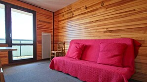 Una habitación con pared de madera, un sofá rojo, una silla y una mesita.