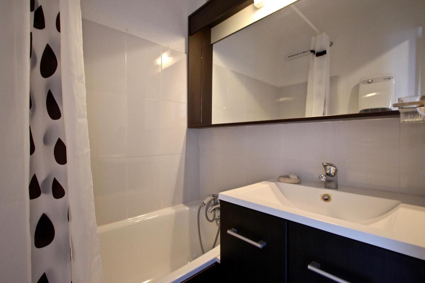 Une salle de bain moderne avec un lavabo blanc, des meubles sombres et un grand miroir.