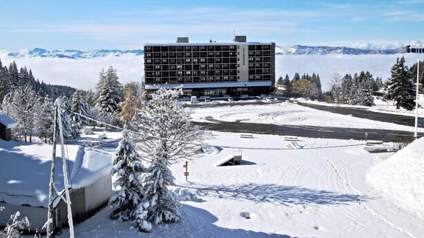 Un edificio moderno con techo plano y varias ventanas, rodeado de árboles cubiertos de nieve y un cielo despejado.