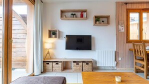 Ein gemütliches Wohnzimmer mit Fernseher, Holzregalen, einer Couch und einem Esstisch.