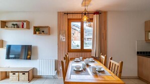 Ein Essbereich mit einem Holztisch, gedeckt für vier Personen, einem Fernseher an der Wand und einem Fenster mit Vorhängen.