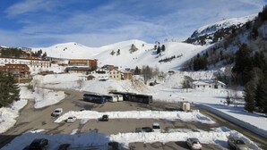 A snow-covered parking lot with several buses and cars, buildings in the background, and a mountainous landscape. - 300m from ski slopes, 7th floor, balcony, tv, 19m², Chamrousse (Chamrousse)
