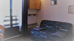 A small, cozy room with a wooden cabinet, a small table, and a couch with a 'keep calm' themed cover. - 50m from ski slopes, 1st floor, view mountain, balcony, tv, ski locker, 20m², Risoul (Risoul)