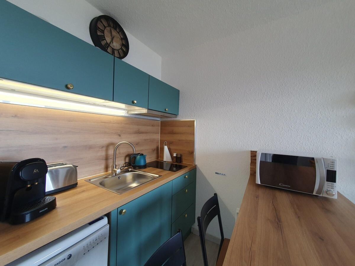 A compact kitchen with teal cabinets, a stainless steel sink, a kettle, a toaster, and a microwave.