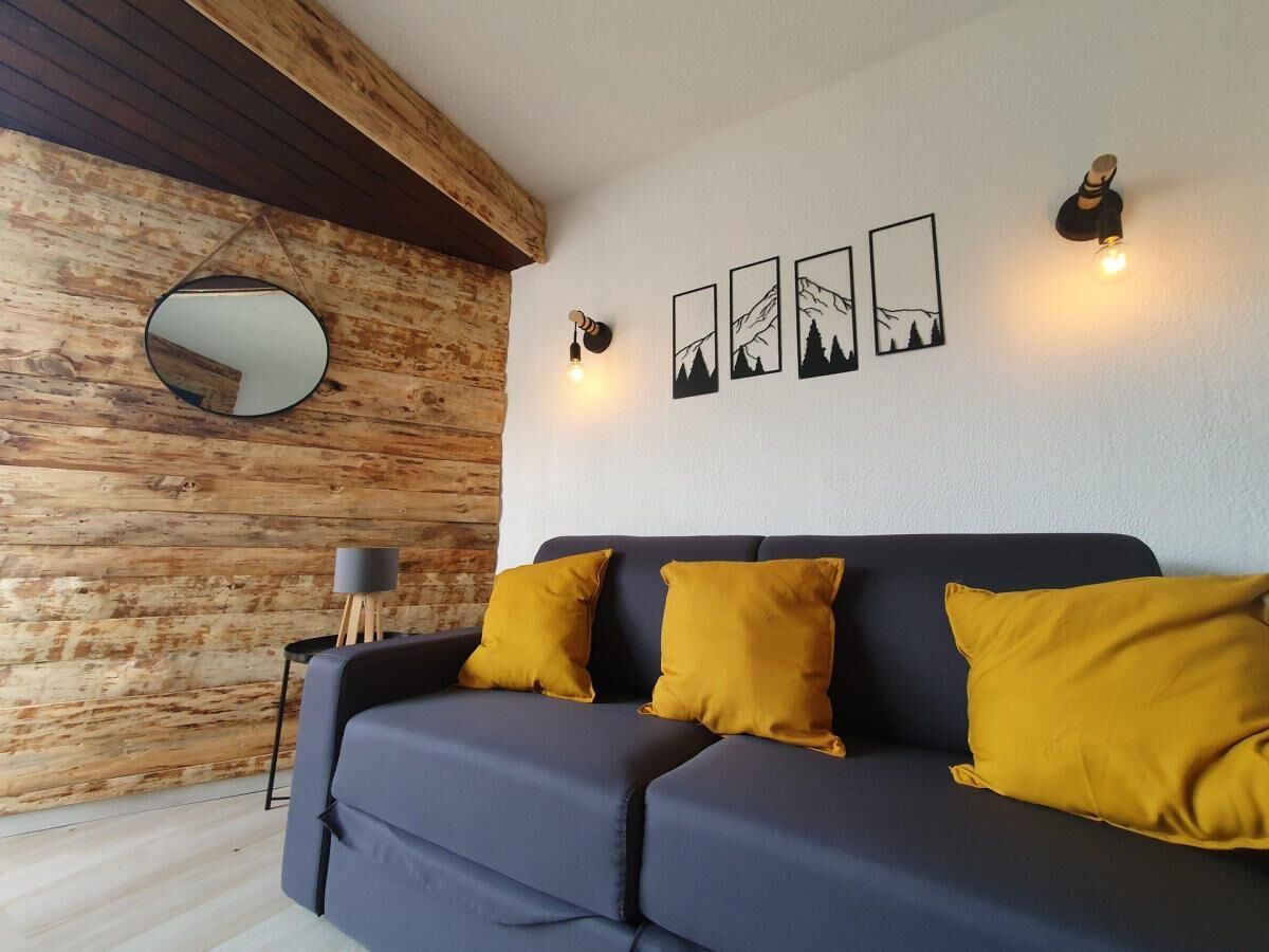 A modern living room with a dark blue sofa, three mustard yellow cushions, a round mirror, and three framed pictures on the wall.