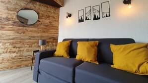 A modern living room with a dark blue sofa, three mustard yellow cushions, a round mirror, and three framed pictures on the wall.