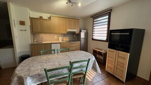A compact kitchen with wooden cabinets, a dining table with chairs, a refrigerator, and a television. - Ground floor, terrace, parking, tv, ski locker, 65m², Serre Chevalier (La Salle-les-Alpes)