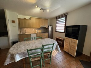 A compact kitchen with wooden cabinets, a dining table with chairs, a refrigerator, and a television. - Ground floor, terrace, parking, tv, ski locker, 65m², Serre Chevalier (La Salle-les-Alpes)