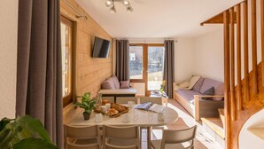 Ein gemütliches Zimmer mit einem runden Esstisch, Stühlen, einer Couch und einem an der Wand befestigten Fernseher.