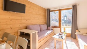 A modern living room with a wooden wall, a sofa, a TV mounted above it, a small table, and a window with curtains.
