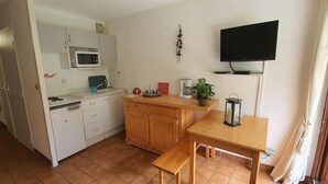 Une cuisine compacte avec des meubles blancs, un four à micro-ondes, une machine à café et une petite table agrémentée d’une lanterne.