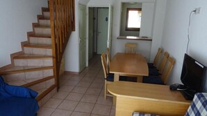 A living room with a wooden staircase, a dining table with chairs, a sofa, and a television. - Chalet, terrace, parking, tv, 62m², Serre Chevalier (La Salle-les-Alpes)