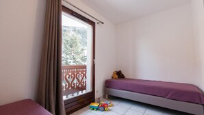 Een kleine kamer met een bed, een raam met gordijnen, een balkon en een speelgoed op de vloer.