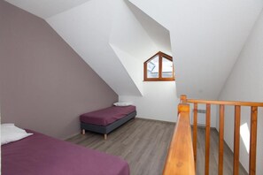 Een kleine kamer met een schuin dak, twee bedden, een houten leuning en een raam.