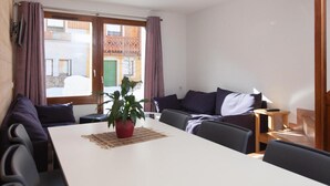 A modern living room with a white dining table, dark sofas, and a potted plant.