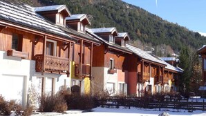 A row of wooden cabins with balconies, set against a snowy mountain backdrop.