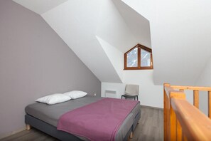 A bedroom with a sloped ceiling, a bed with pillows, a chair, and a window.