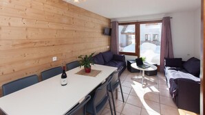 Una habitación acogedora con pared de madera, una mesa de comedor con sillas, un sofá y una mesita redonda con una computadora portátil.