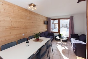 Tunnelmallinen huone, jossa on puuseinä, ruokapöytä tuoleineen, sohva ja pieni pyöreä pöytä, jonka päällä on kannettava tietokone.