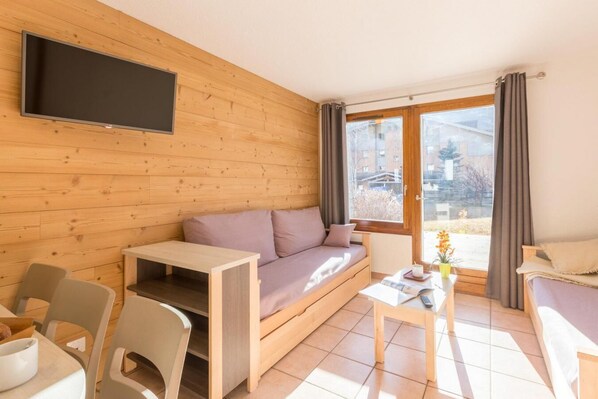 A modern living room with a wooden wall, a sofa, a TV mounted above it, a small table, and a window with curtains.