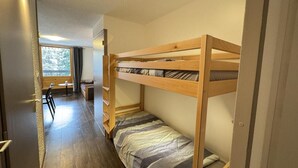 Quarto com beliche, piso de madeira, uma pequena mesa e uma cadeira.