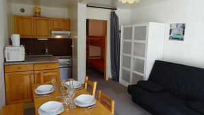 A compact kitchen with wooden cabinets, a microwave, and a stove. There is a dining table set with plates and glasses. A black sofa is in the living area, and a white cabinet is visible. - 50m from resort center, 5th floor, balcony, tv, ski locker, 28m², Serre Chevalier (La Salle-les-Alpes)
