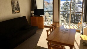 A living room with a sofa, a wooden table, and a TV on a cabinet. - 50m from resort center, 5th floor, balcony, tv, ski locker, 28m², Serre Chevalier (La Salle-les-Alpes)