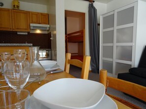 A compact kitchen with wooden cabinets, a dining table with white plates and glasses, and a bunk bed in the background.